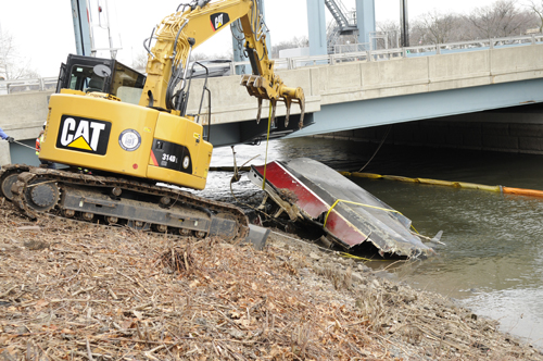 Photo courtesy Chris Brooks From top.: PVSC excavator re-positions boat, then crane begins to lift vessel, and deposits mangled remains into flatbed trailer under highway.