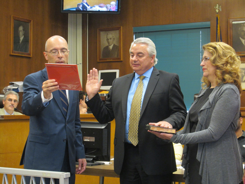 Photo by Ron Leir With his wife, Maria, holding the Bible, John Peneda (c.) is sworn in as new assessor by Mayor Alberto Santos at June 25 council session.